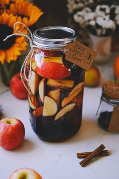 a jar filled with apples and cinnamons on top of a table next to sunflowers