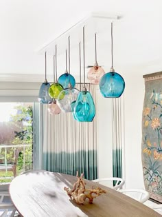 a dining room table and chairs with colorful glass hanging from the ceiling