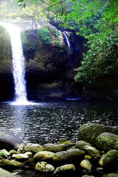 a large waterfall in the middle of a forest filled with rocks and water surrounded by greenery