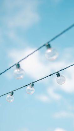 several light bulbs are hanging on a wire against a blue sky with clouds in the background