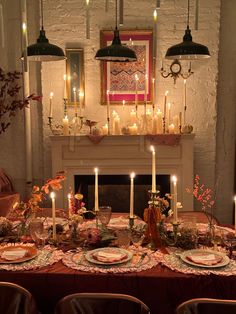 a table with plates and candles in front of a fireplace