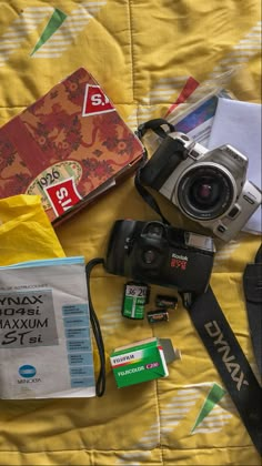 a camera and some other items are laying on a bed with a yellow sheet behind it