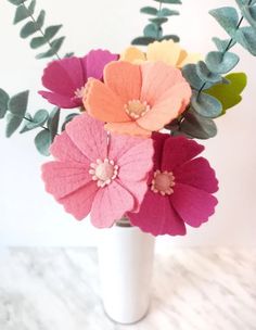 a white vase filled with colorful flowers on top of a marble counter next to green leaves