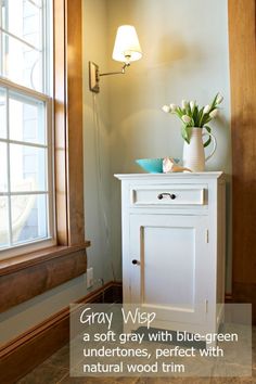 a white cabinet sitting next to a window with a vase filled with flowers on top of it