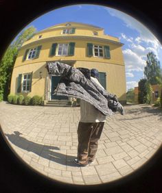 a man standing in front of a yellow building holding a large piece of luggage on his back