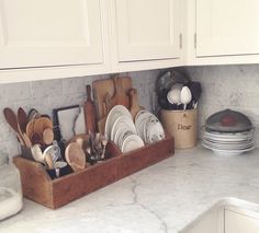 a kitchen counter with dishes and utensils in a wooden tray on top of it