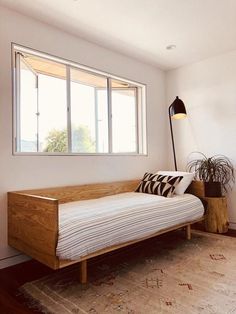 a room with a bed, lamp and rug on the floor in front of a window