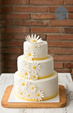 a three tiered cake with white and yellow flowers