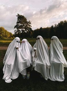 three people dressed in white cloths sitting on the grass with trees in the background