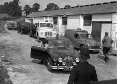 an old black and white photo of men standing in front of parked cars on a dirt road