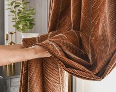 a person is holding up a brown curtain in front of a table with a potted plant on it