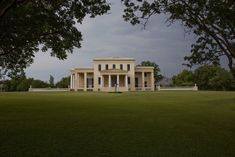 a large white house sitting in the middle of a lush green field under a cloudy sky