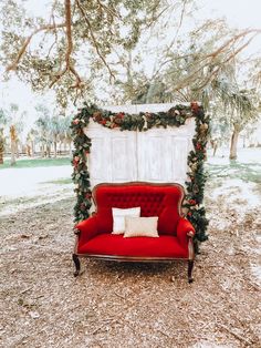 a red couch sitting in the middle of a field next to a white door with greenery on it