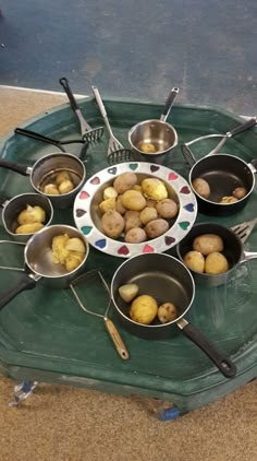 several pots and pans with potatoes in them on a green tray next to utensils