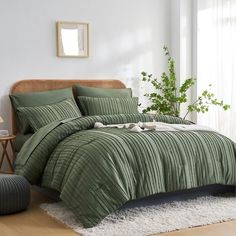 a bed with green comforter and pillows in a room next to a plant on the floor