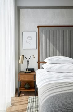 a bed sitting next to a window with white curtains and pillows on top of it