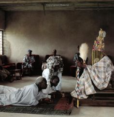 several people sitting and standing around in a room with rugs on the floor, one person laying down