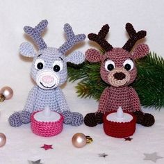 two crocheted reindeers sitting next to each other with christmas decorations around them