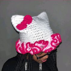 a woman wearing a knitted hello kitty hat with pink flowers on her head and cell phone in her hand