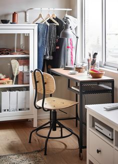 a chair sitting in front of a desk with clothes hanging on the rack behind it