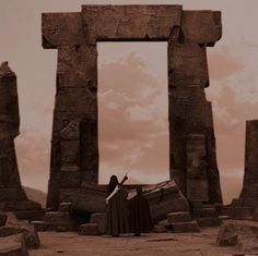 a man standing in front of two large stone pillars on top of a dirt field