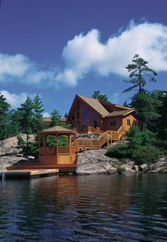 a house sitting on top of a lake next to a wooden dock in front of a forest