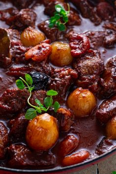 a bowl filled with meat and potatoes on top of a wooden table next to green leaves