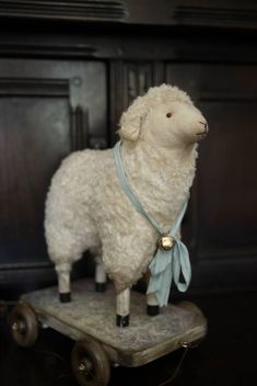 a white sheep with a blue ribbon on it's neck standing on a wooden cart