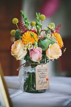 a vase filled with lots of flowers on top of a white tablecloth covered table