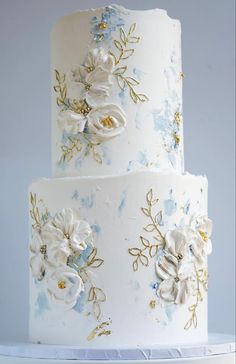 a three tiered wedding cake with white and blue flowers on the top, sitting on a stand