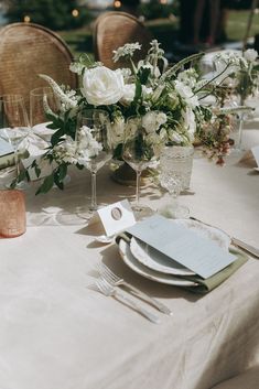 the table is set with white flowers and place settings