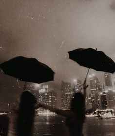 two people holding open umbrellas in front of a cityscape at night time