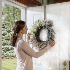 a woman is holding a wreath on the front door to open it and looking outside