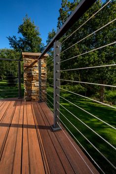 a wooden deck with metal railings and stone wall on the other side, surrounded by green grass