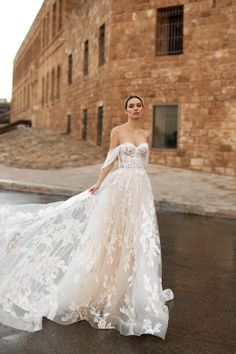 a woman in a white wedding dress standing on the street with an old brick building behind her