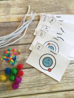 four different colored pom poms are on the table next to some paper and scissors