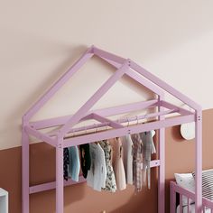 a baby's room with pink walls and clothes hanging on the rack in front of it