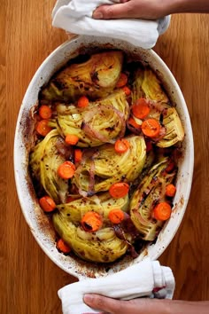 a dish with carrots, onions and other vegetables in it on a wooden table