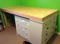 a white desk with lots of drawers in a green room next to a book shelf