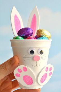 a hand holding up a cup filled with chocolate eggs and an easter bunny's face