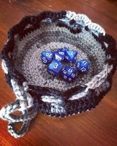 a crocheted basket with blue dices in it on a wooden table top