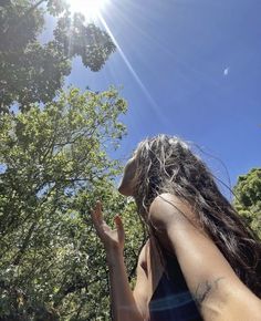 a woman standing in front of trees with her hand up to the sky and sun shining on her face