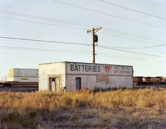 an old building sitting in the middle of a dry grass field with a train passing by