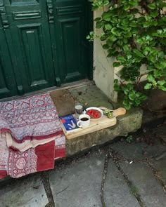 a table with food on it sitting in front of a green door next to a brick walkway