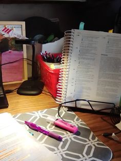 a laptop computer sitting on top of a desk next to a pile of papers and pens