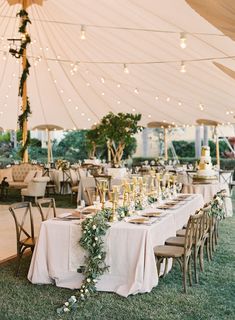 an outdoor tent with tables and chairs covered in white linens, greenery and candles