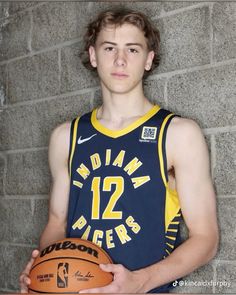 a young man holding a basketball in front of a brick wall