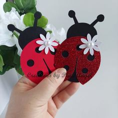 two ladybug magnets with white flowers in the middle and one has red glitter on it