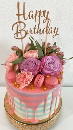 a birthday cake decorated with pink flowers and macaroons on a gold plated stand