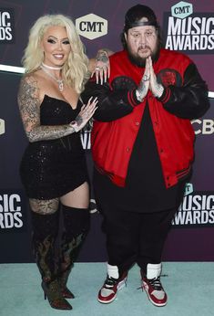 two people standing on a blue carpet with one person wearing a red jacket and the other in black